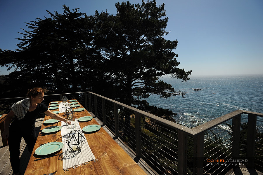 A catering vendor is decorating the outdoor dinning table in an outside balcony facing to the ocean at a wind and sea wedding in big sur