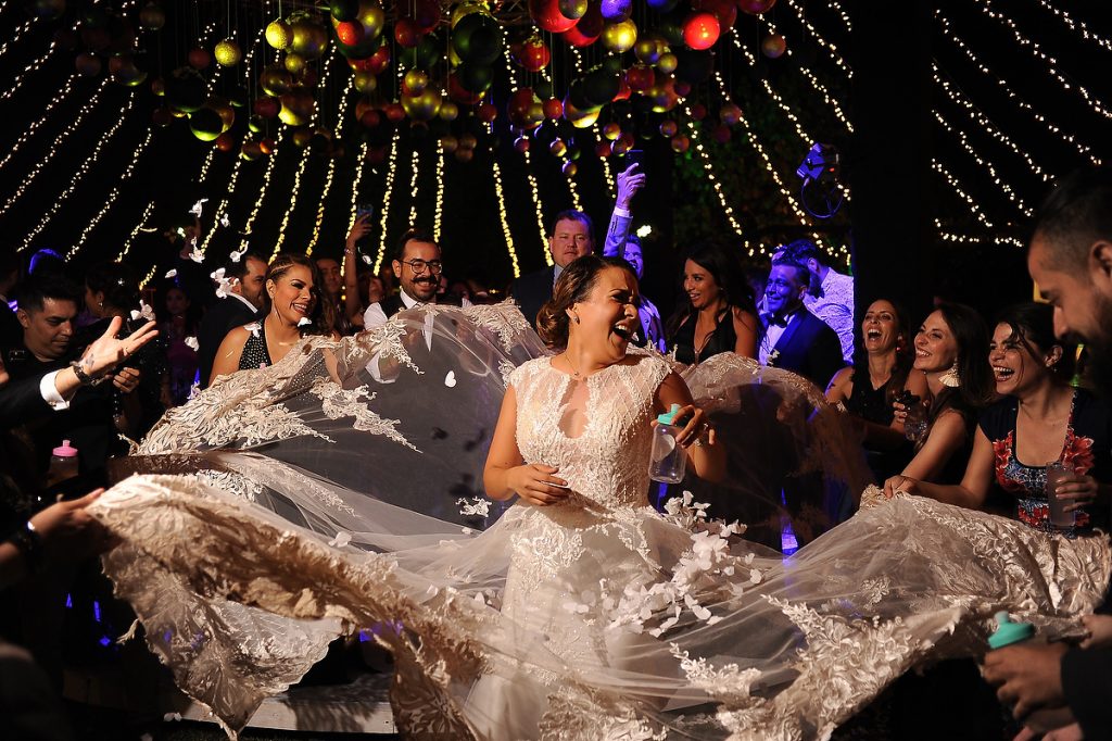 A group of friends of the bride hold the brides wedding dress train and toss it up and down while everybody smiles during the wedding reception at decantos vinicola